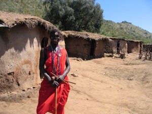 案内してくれたマサイの青年。学校に通い英語を学んだひとが観光客の相手をする。背後にあるのはマサイの家。牛の糞を乾かしたものを用い建てられる。家の建設は女性の仕事とか。