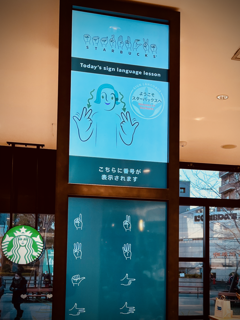 東京・国立駅内にある「スターバックス コーヒー nonowa国立店」は、手話によるコミュニケーションを採り入れている日本初の店舗。聴覚障がいのある従業員の方が働いており、デジタルサイネージほか店内各所にハンドサインが配され、壁には手話をモチーフとしたアート作品も飾られる。（撮影＝bg）